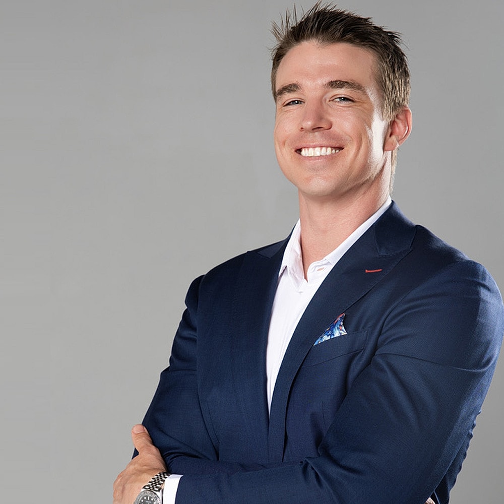 Smiling man in a blue suit, arms crossed.