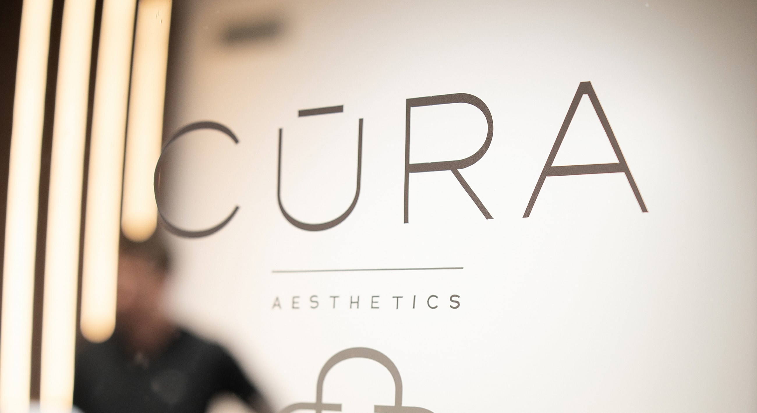 CŪRA Aesthetics logo on a wall.